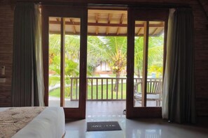 A room with a bed, a sliding glass door leading to a balcony with a view of palm trees. - Maruti Beach Villas (Bali)