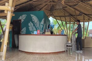 A reception area with a curved counter, a bamboo ceiling, and a large plant. - Maruti Beach Villas (Bali)