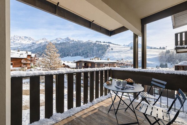 A balcony with a view of snow-covered mountains and a wooden deck.