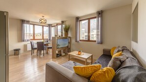 A modern living room with a sofa, TV, dining table, and large windows.