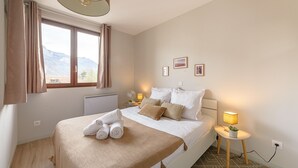 A neatly made bed with a beige blanket, a bedside lamp, and a small table with a plant.