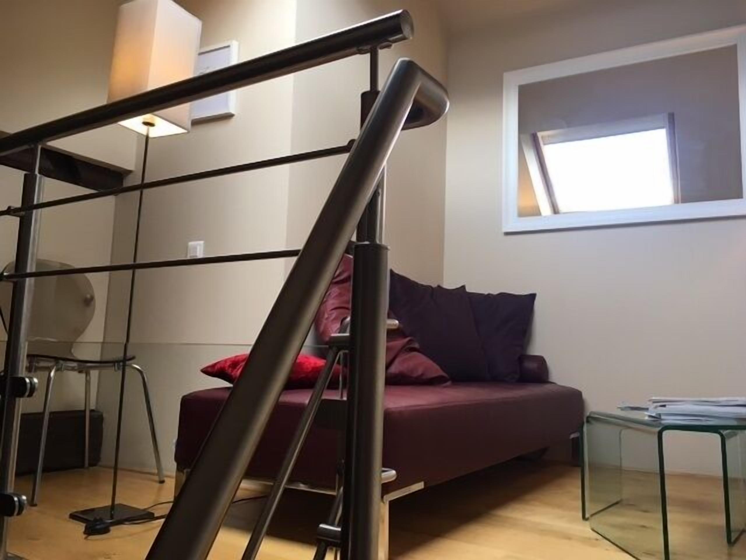 A modern living room with a glass coffee table, a sofa with red cushions, and a staircase with a metal railing.