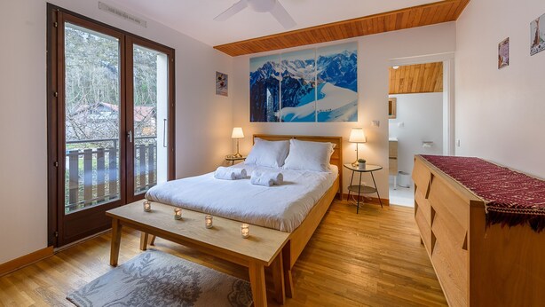 Ein Schlafzimmer mit Bett, Nachttischen, Deckenventilator, großem Fenster und Blick ins Freie.