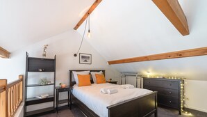 A bedroom with a dark wooden bed, white bedding, and orange pillows. There is a nightstand with a lamp, a dresser, and a shelf with decorative items. - Le Balcon des Lys - Centre village, 4p (Veyrier-du-Lac)