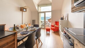 A modern kitchen with a large island, a dining area with a table set for four, and a bright room with a view of the sea. - Le Balcon des Lys - Centre village, 4p (Veyrier-du-Lac)