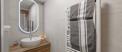 A bathroom with a round mirror, a white sink, a wooden vanity, and a towel rack with a striped towel.