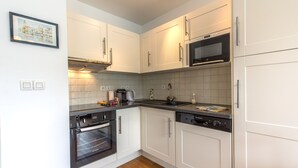 A modern kitchen with white cabinets, a built-in oven, microwave, and dishwasher. - Le Studio Rivage - Surplombant le lac (Duingt)