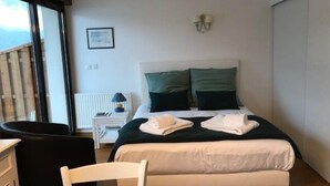 A bedroom with a bed, a nightstand, a chair, and a window. - Le Studio Rivage - Surplombant le lac (Duingt)