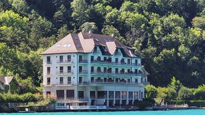 A multi-story building with balconies, situated by a body of water, surrounded by greenery. - Le Studio Rivage - Surplombant le lac (Duingt)