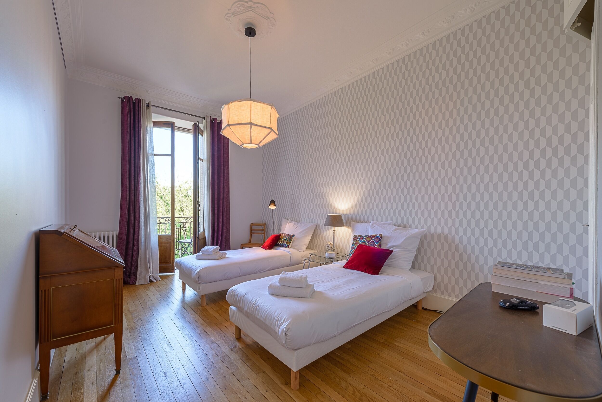 Une chambre avec deux lits, un bureau en bois, une table et une fenêtre avec des rideaux.
