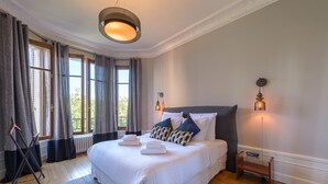 A spacious bedroom with a large bed, a standing heater, and a bedside table with a lamp.