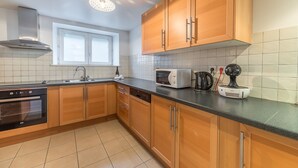 A modern kitchen with wooden cabinets, a built-in oven, a microwave, and a coffee maker.