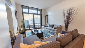 A modern living room with a large window, a grey sofa, a brown sofa, a coffee table, and a decorative plant.