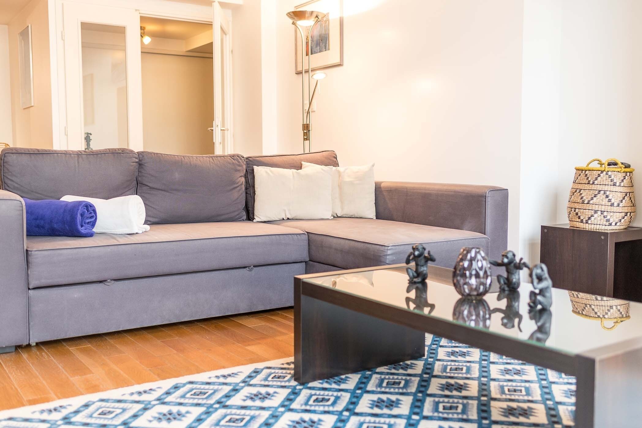 Een moderne woonkamer met een grijze modulaire bank, een glazen salontafel en een vloerkleed met dessin.