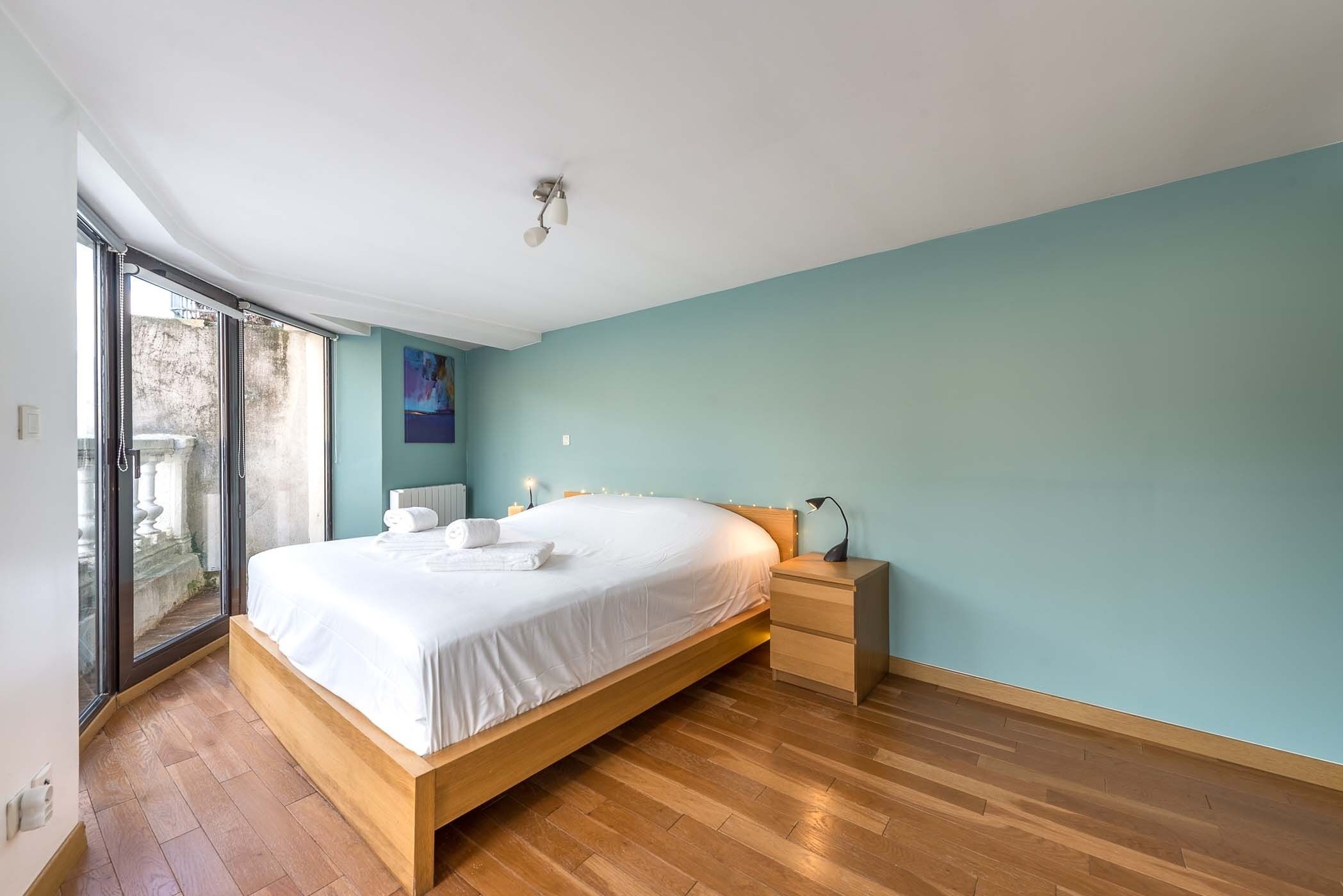 A modern bedroom with a wooden bed, a nightstand, and a large window.