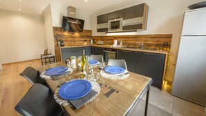 A modern kitchen with dark cabinets, a stainless steel refrigerator, and a wooden dining table set with blue plates and white napkins.