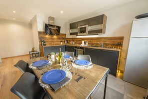 Eine moderne Küche mit dunklen Schränken, einem Edelstahlkühlschrank und einem Holzespeisetisch, gedeckt mit blauen Tellern und weißen Servietten.