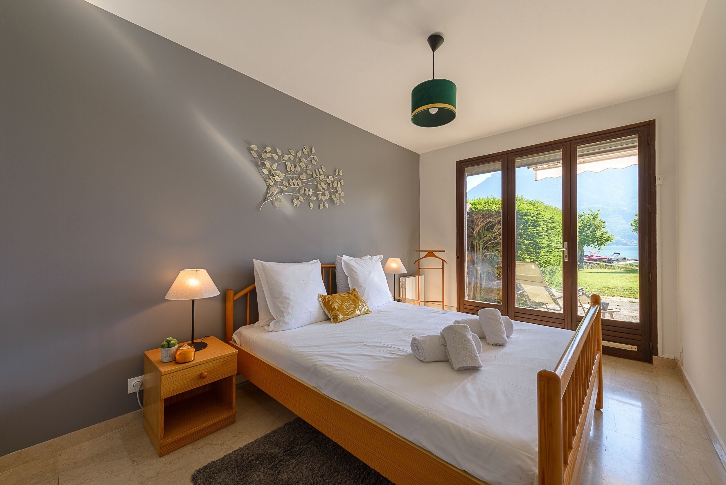 A bedroom with a bed, bedside tables, a lamp, and a view of the outdoors.