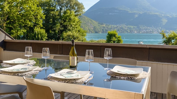 Ein Esstisch aus Glas mit Weinglas, mit Blick auf einen See und Berge.
