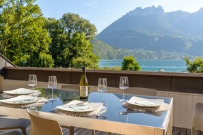 An outdoor dining area with a table set for six, overlooking a lake and mountains. - Loft Azur - terrasse vue lac, plage privée pour les résidents (Duingt)
