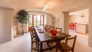 A dining area with a long wooden table, chairs, and a red bowl centerpiece. There is a potted plant and a stone wall. - La Grande Mélodie - Maison familiale avec jardin (Saint-Jorioz)