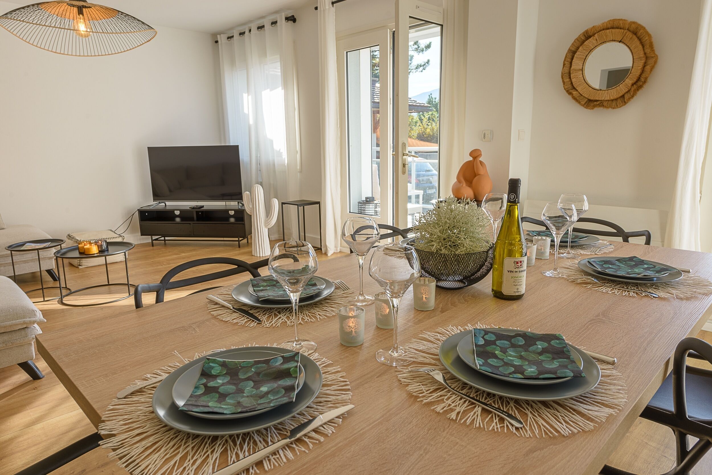 Een eetgedeelte met een houten tafel voor vier personen, omringd door stoelen. Een televisie is zichtbaar op de achtergrond, en een raam biedt uitzicht op het omliggende landschap.