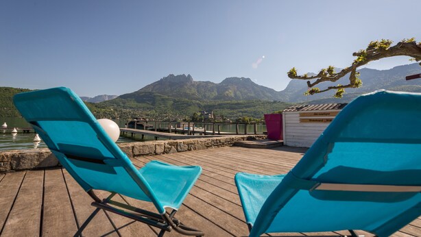 Two turquoise lounge chairs on a wooden deck overlooking a mountain and a body of water.
