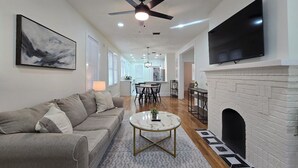 A modern living room with a gray sofa, a round coffee table, a fireplace, and a flat-screen TV mounted on the wall. - Bright & Modern Prime Location (Jacksonville)