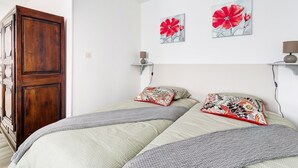 A bedroom with two beds, a wooden wardrobe, and two wall-mounted lamps.