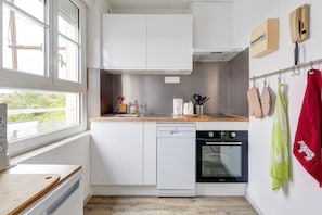 Una cocina compacta con armarios blancos, lavavajillas, horno y ventana que proporciona luz natural.