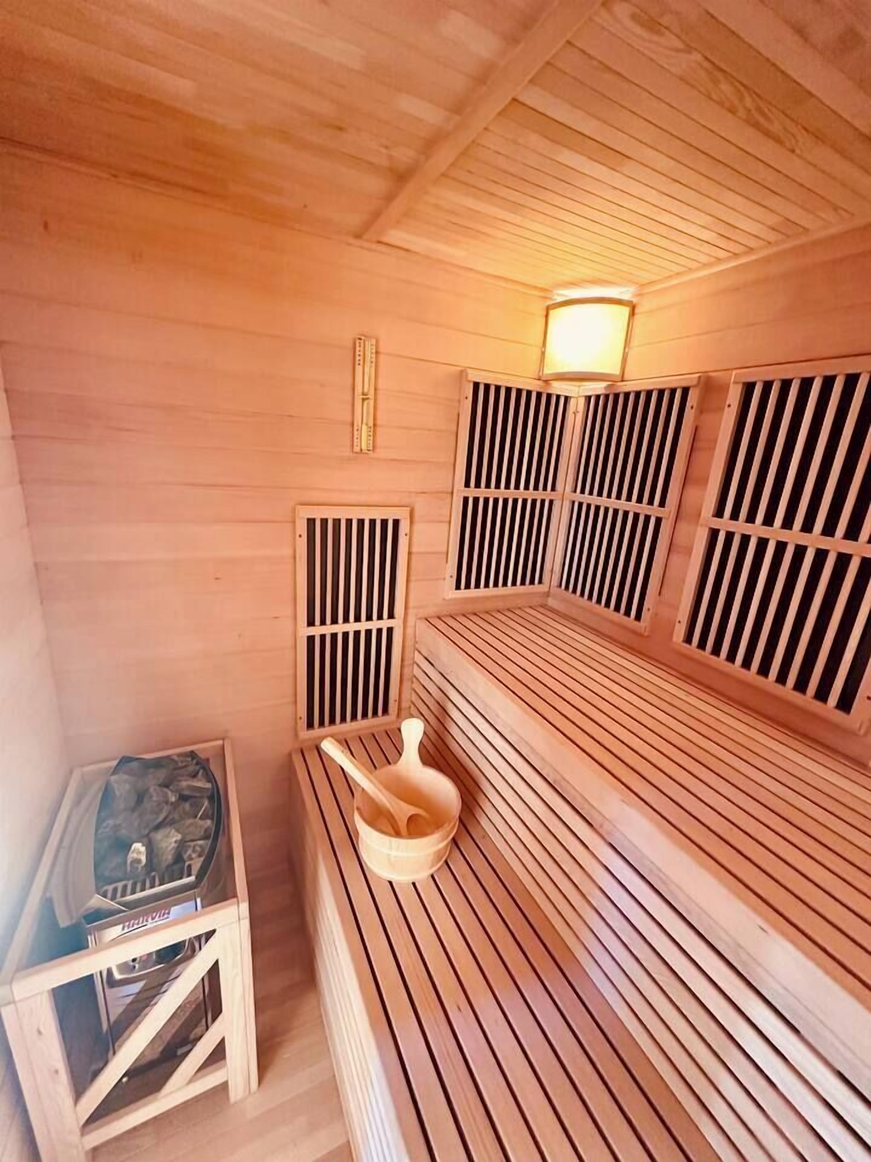 A sauna with wooden benches, a wooden table with a heater, and a wall-mounted light fixture.