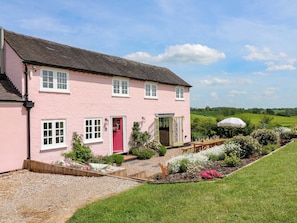 A pink house with a red door, white windows, and a garden with flowers and a bench.
