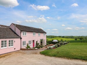 A pink house with a red door, a gravel driveway, and a grassy field in the background. - Gapstile (Rugeley)