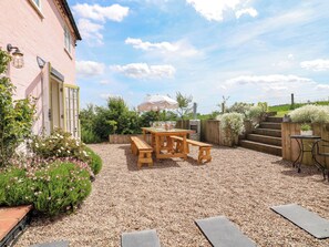 Eine Terrasse mit Holztisch und -bänken, einem Steinofen und einem Kiesgrund.