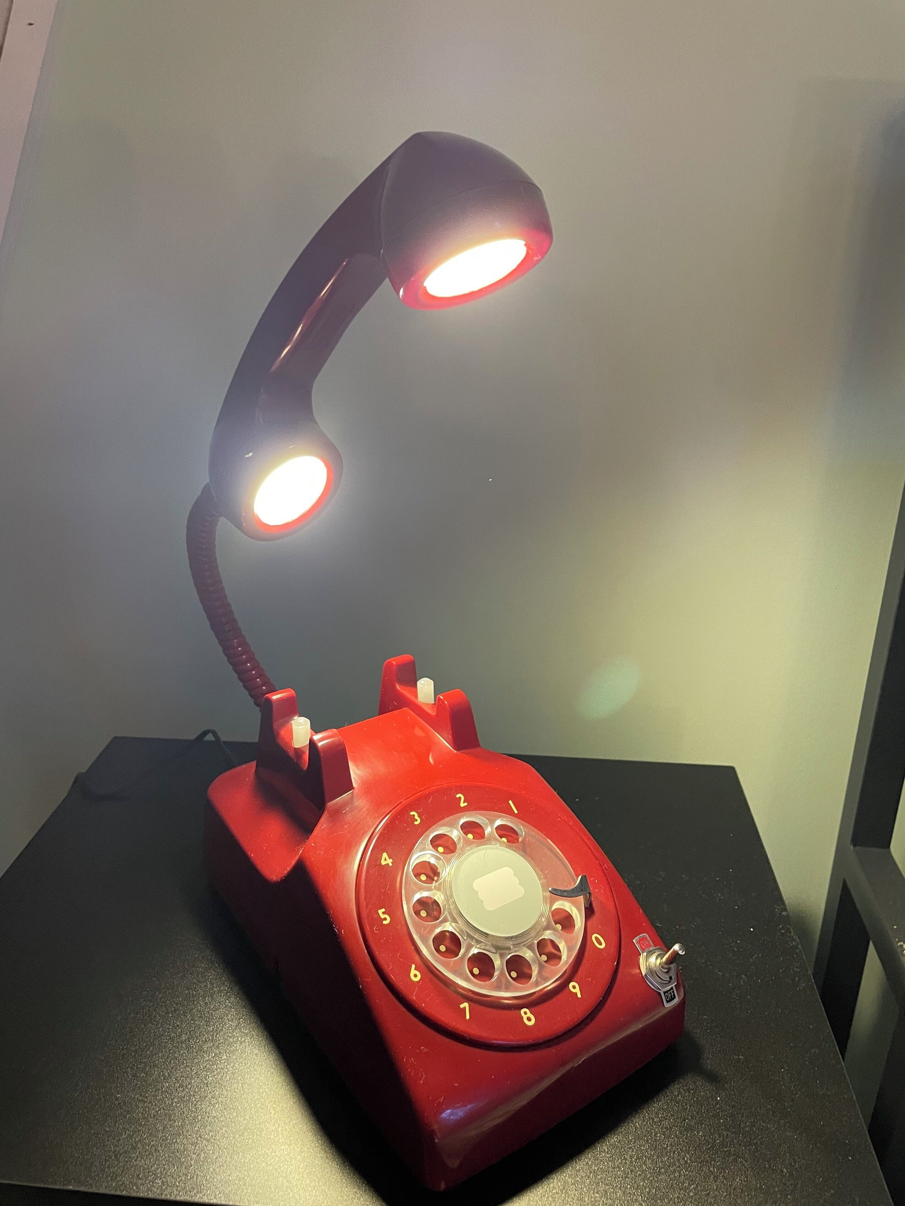 A red telephone with a desk lamp attached, placed on a black surface.