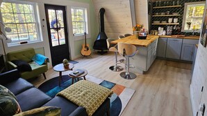 Un espacio habitable estilo loft con techo alto, una mesa de comedor, una cocina con estufa negra y una guitarra.