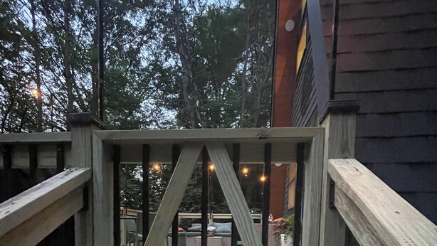 A wooden staircase leading to a deck with a metal gate, surrounded by trees and a building with a dark exterior.
