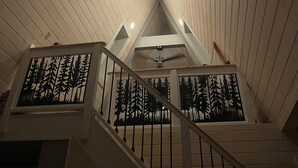 Un interior de madera con una escalera, un ventilador de techo e iluminación empotrada.