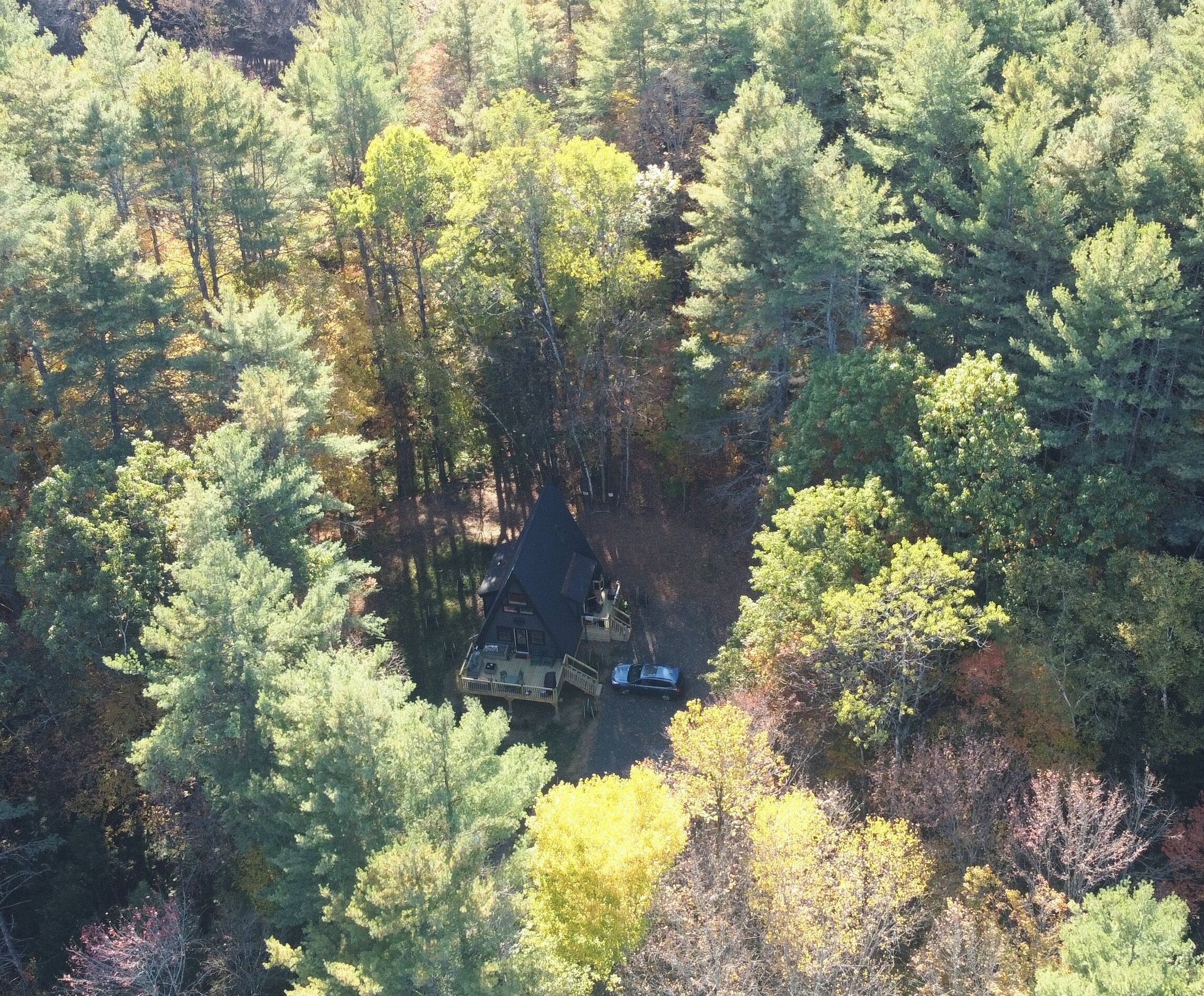 An aerial view of a cabin surrounded by dense forest.