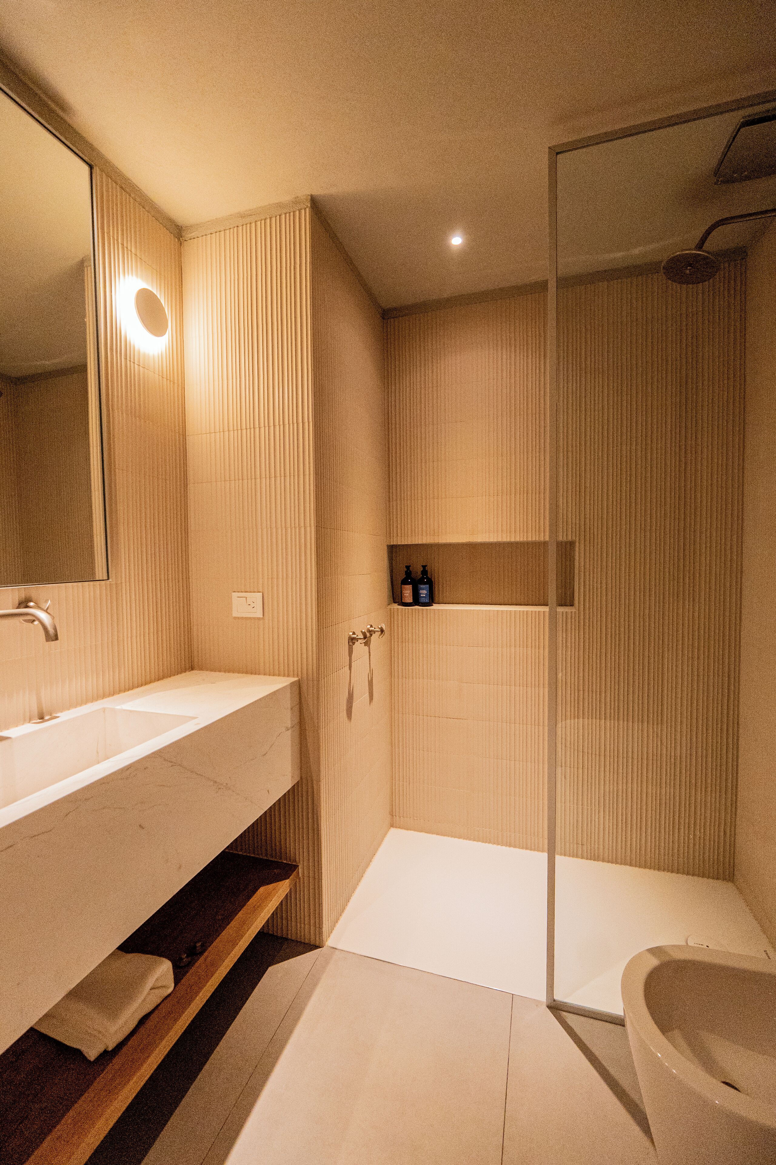 A modern bathroom with a large mirror, a sink, a shower, and a toilet.