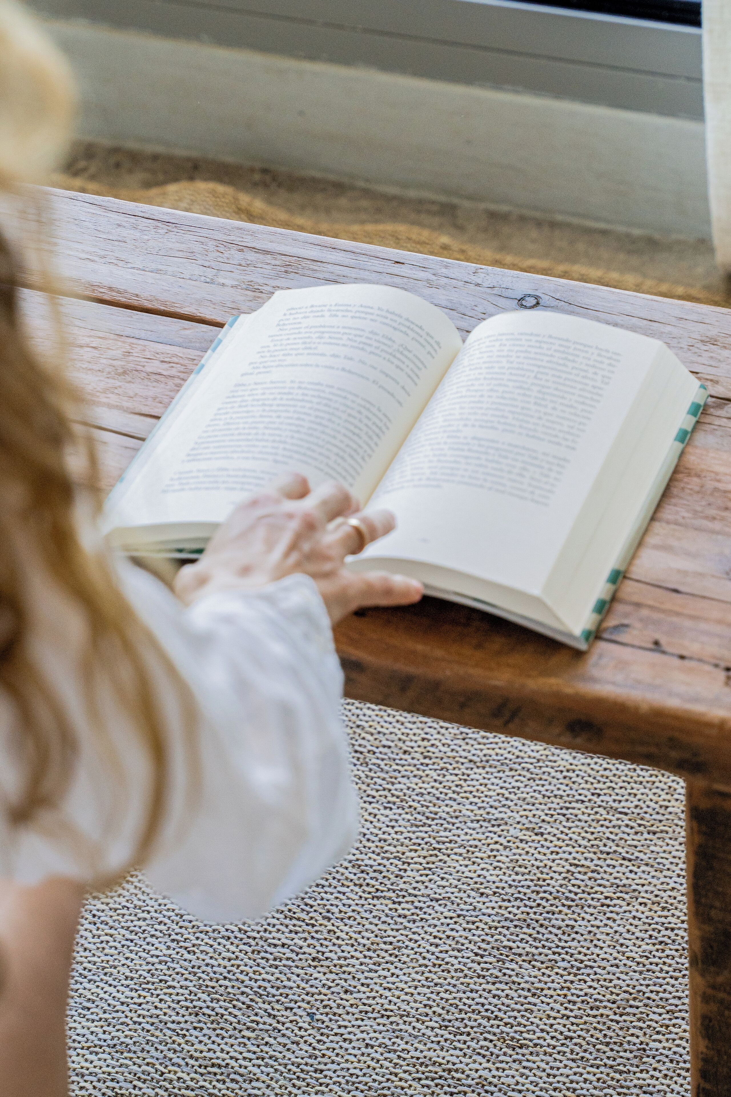 A person reading a book on a wooden bench.