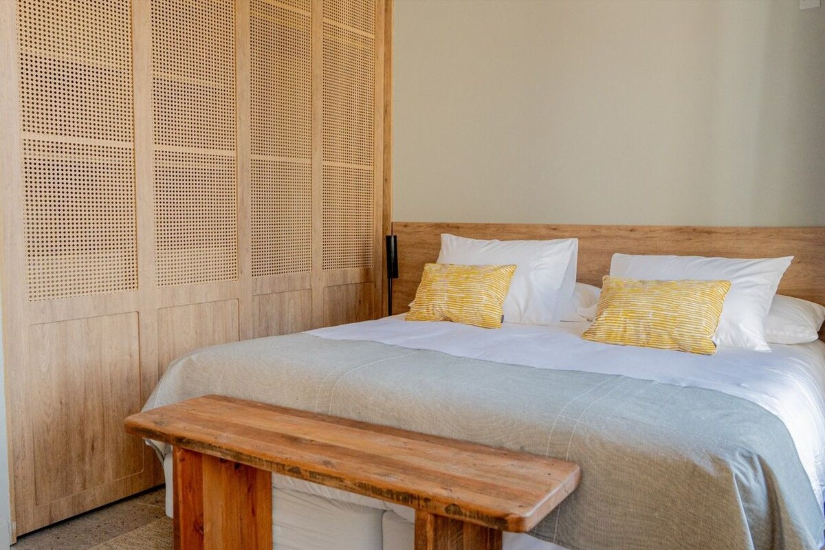 Una cama con cabecera de madera, ropa de cama blanca y dos almohadas amarillas.