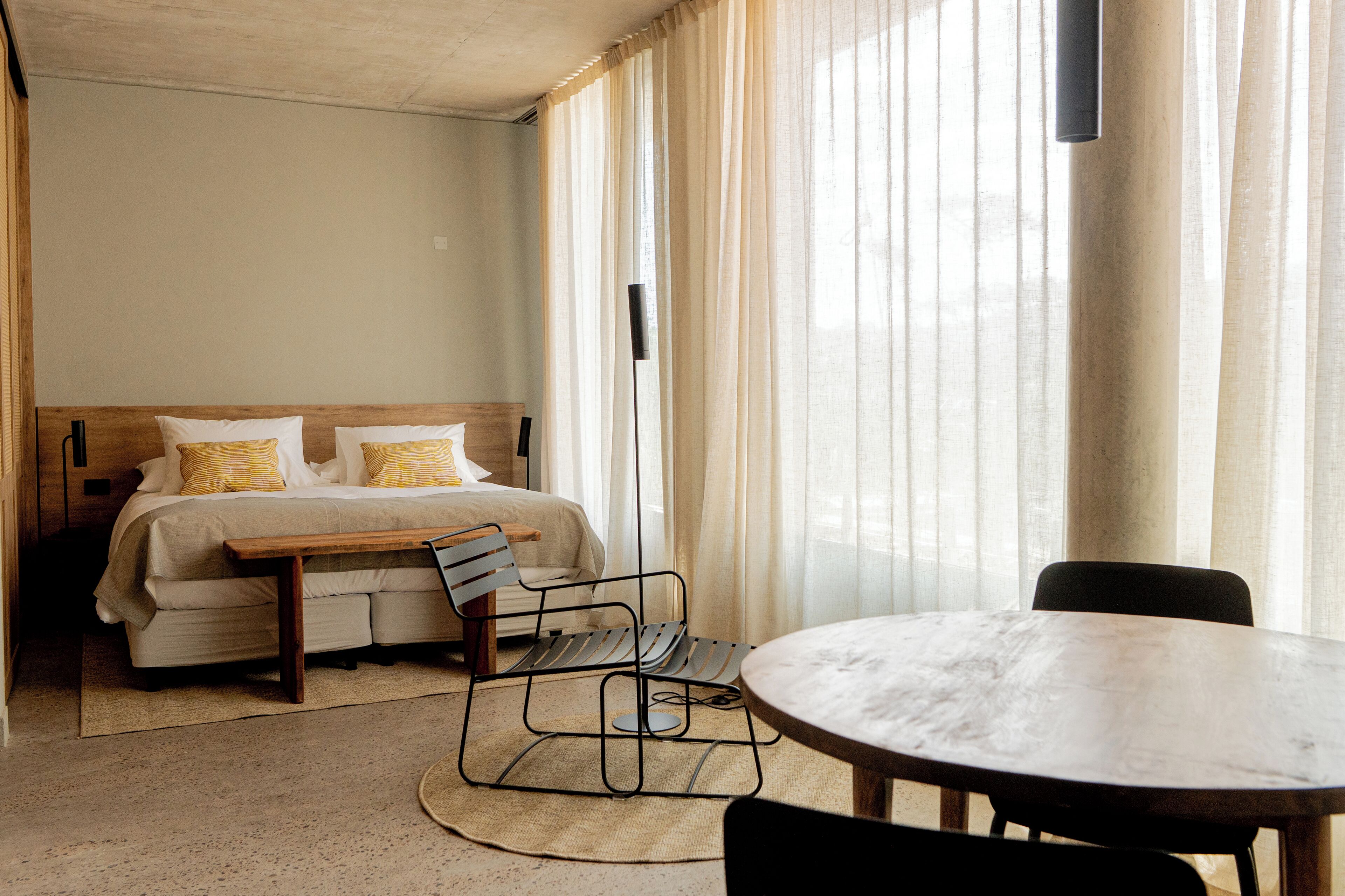 A hotel room with a bed, a wooden bench, a round table, and a chair.