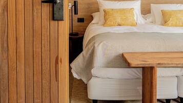 Una puerta de madera con el número 209, una cama con ropa de cama blanca y almohadas a rayas, una mesita de noche y una lámpara.
