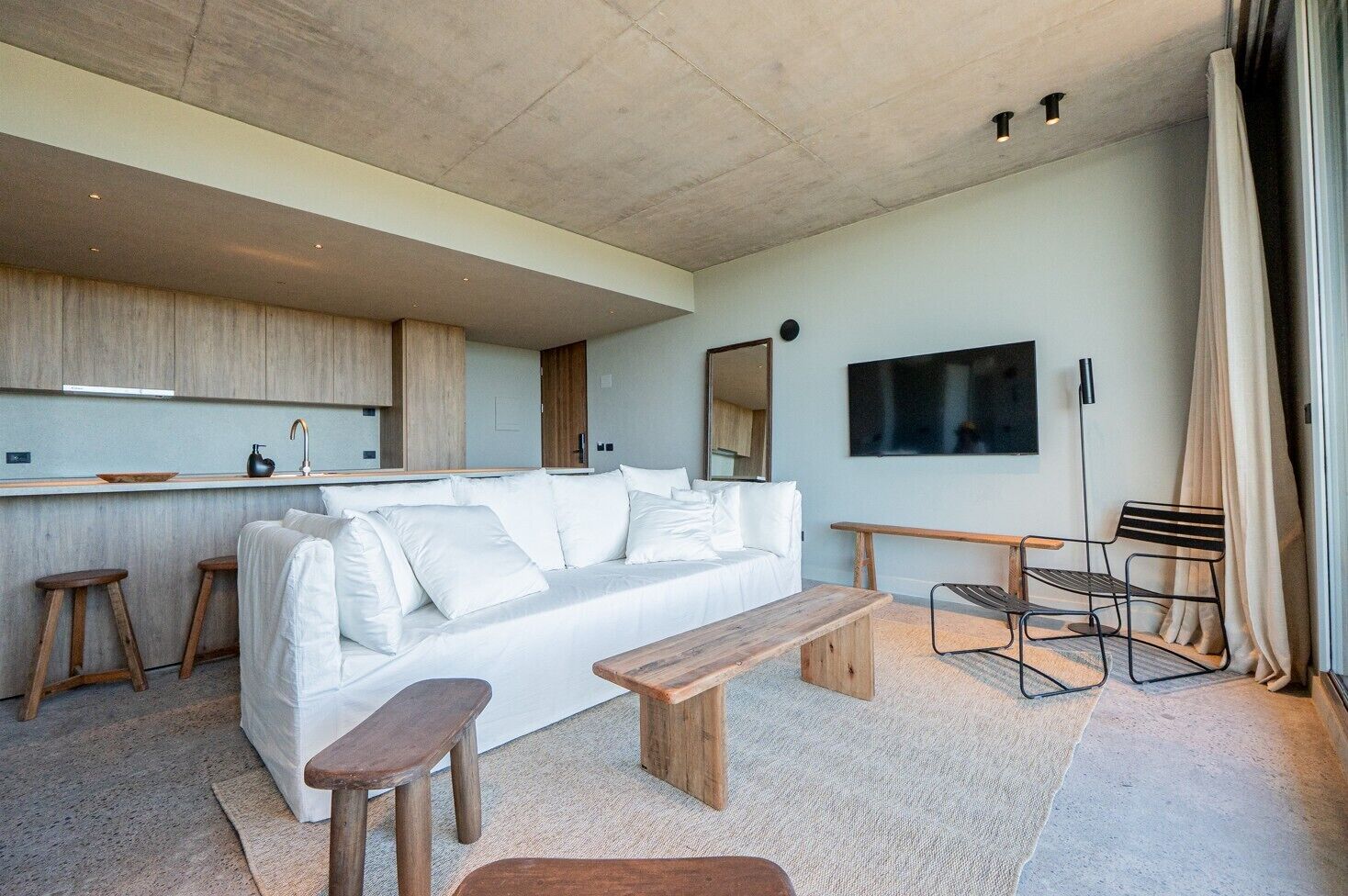 Ein modernes Wohnzimmer mit Sofa, Holzschemeln, einer Bank, einem Flachbildfernseher und einer Küchenzeile.