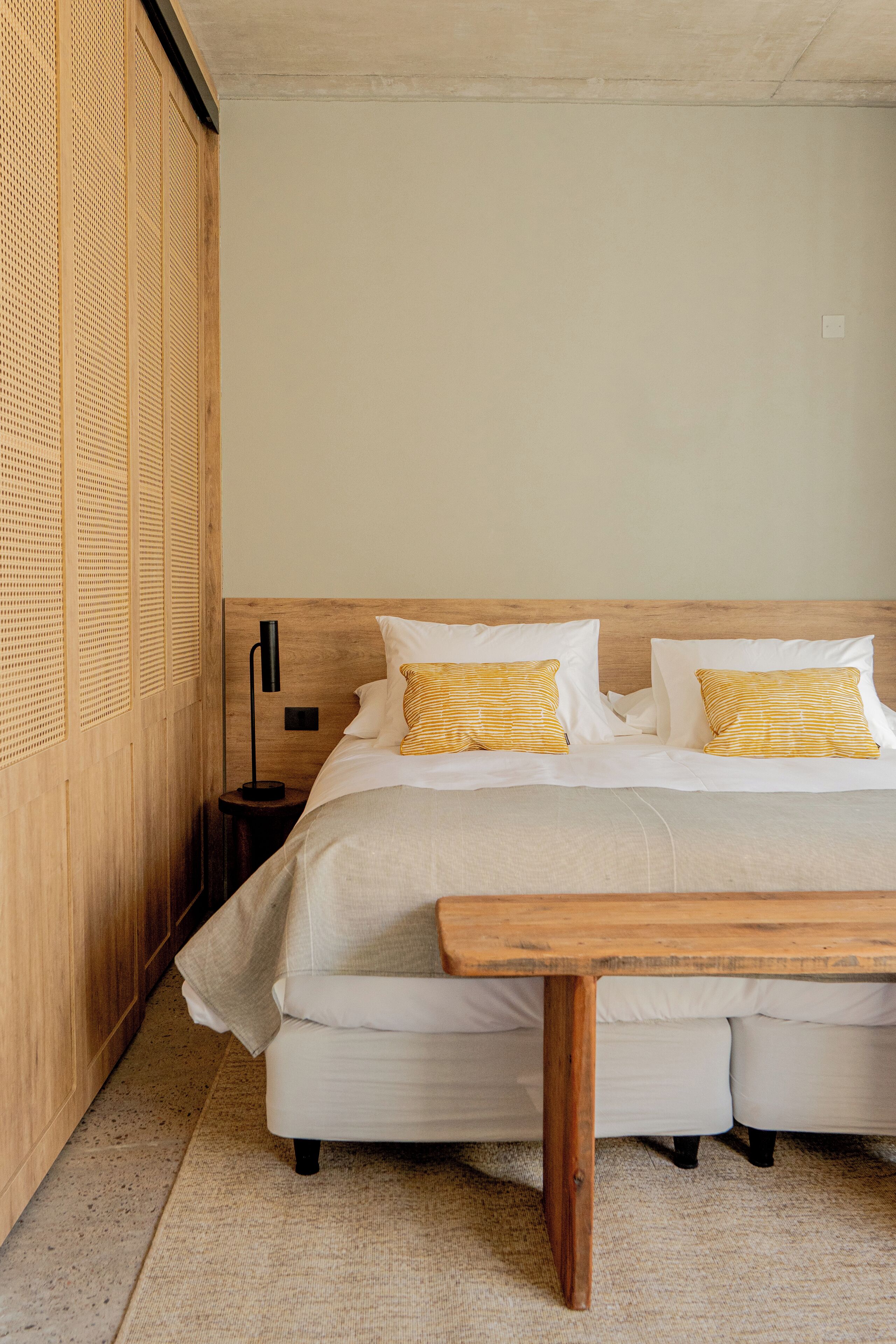 A neatly arranged bedroom with a large bed, a bedside table, and a wooden bench.