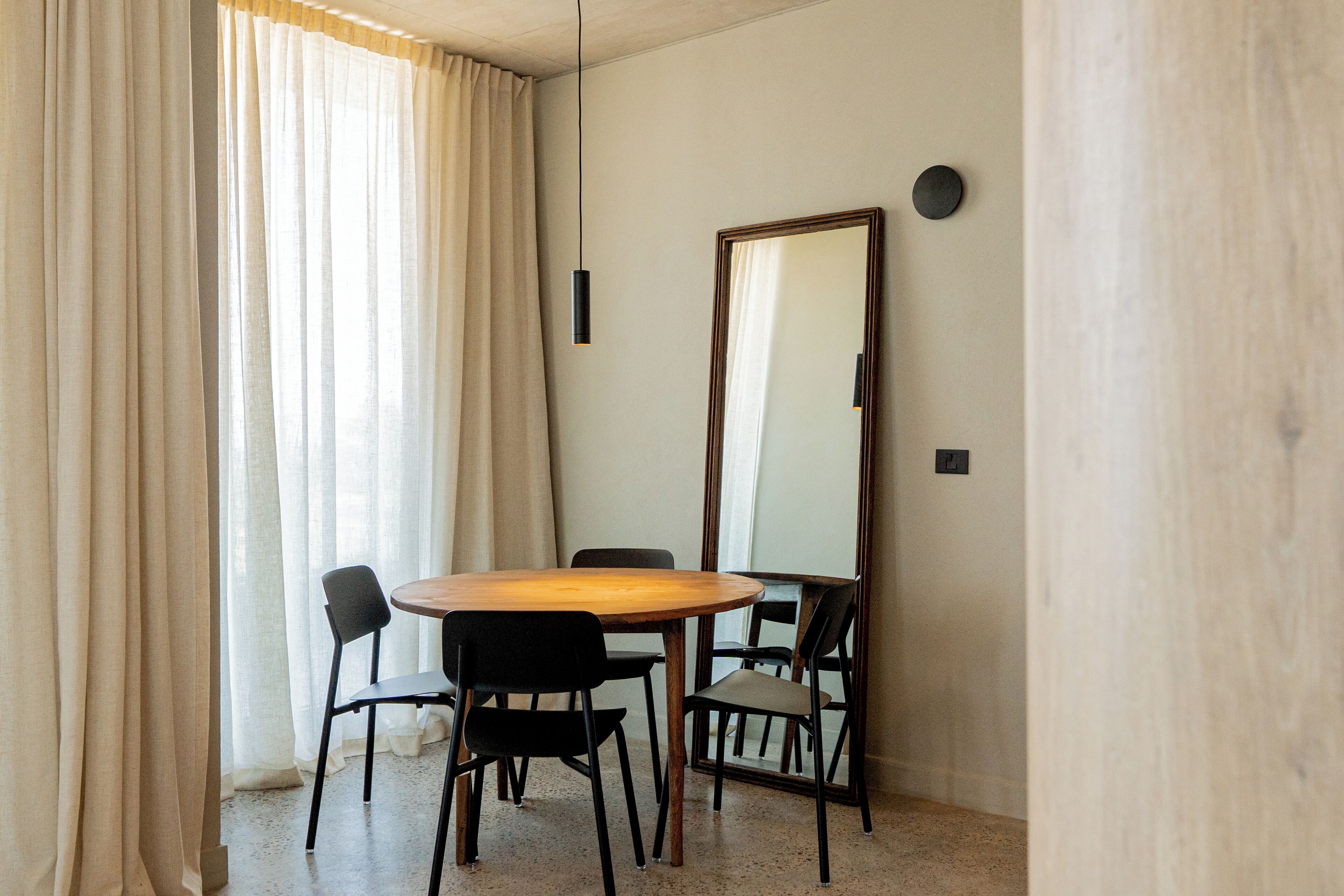 A dining area with a round table, four chairs, a large mirror, and a hanging light fixture.