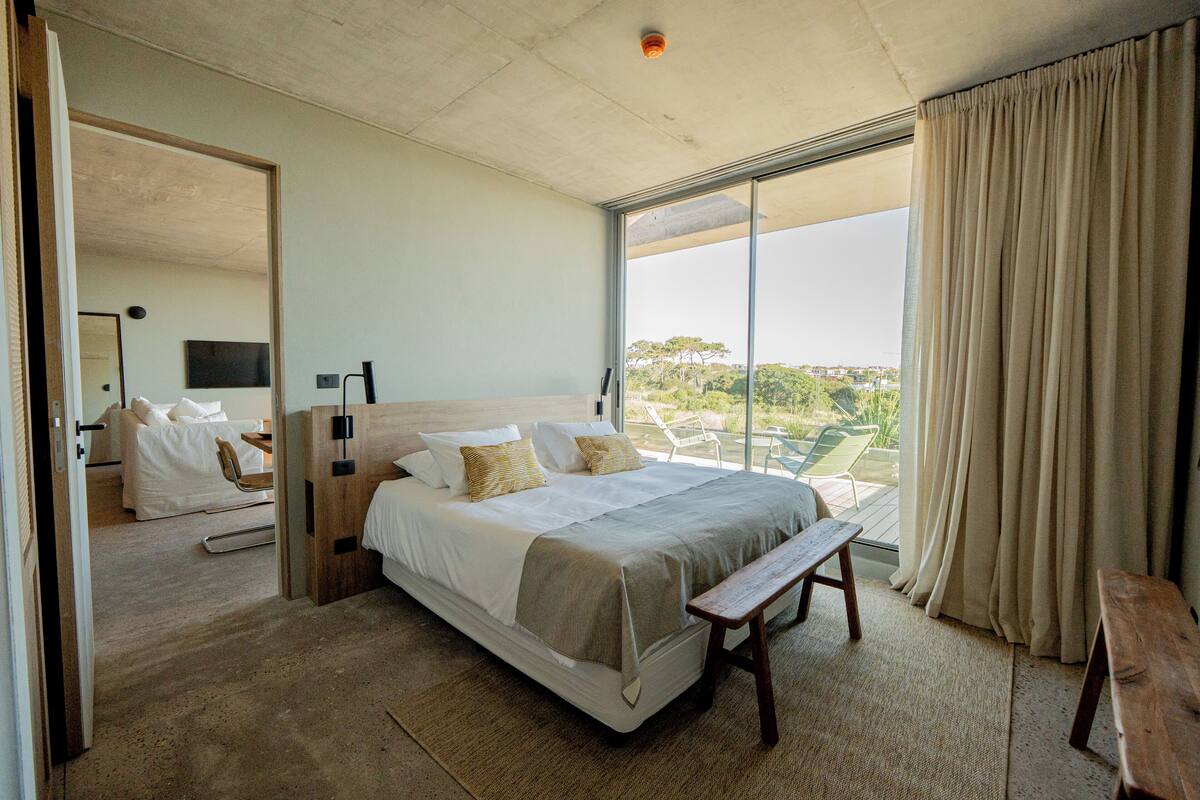 A spacious bedroom with a large bed, a bench, and a view of the outdoors.