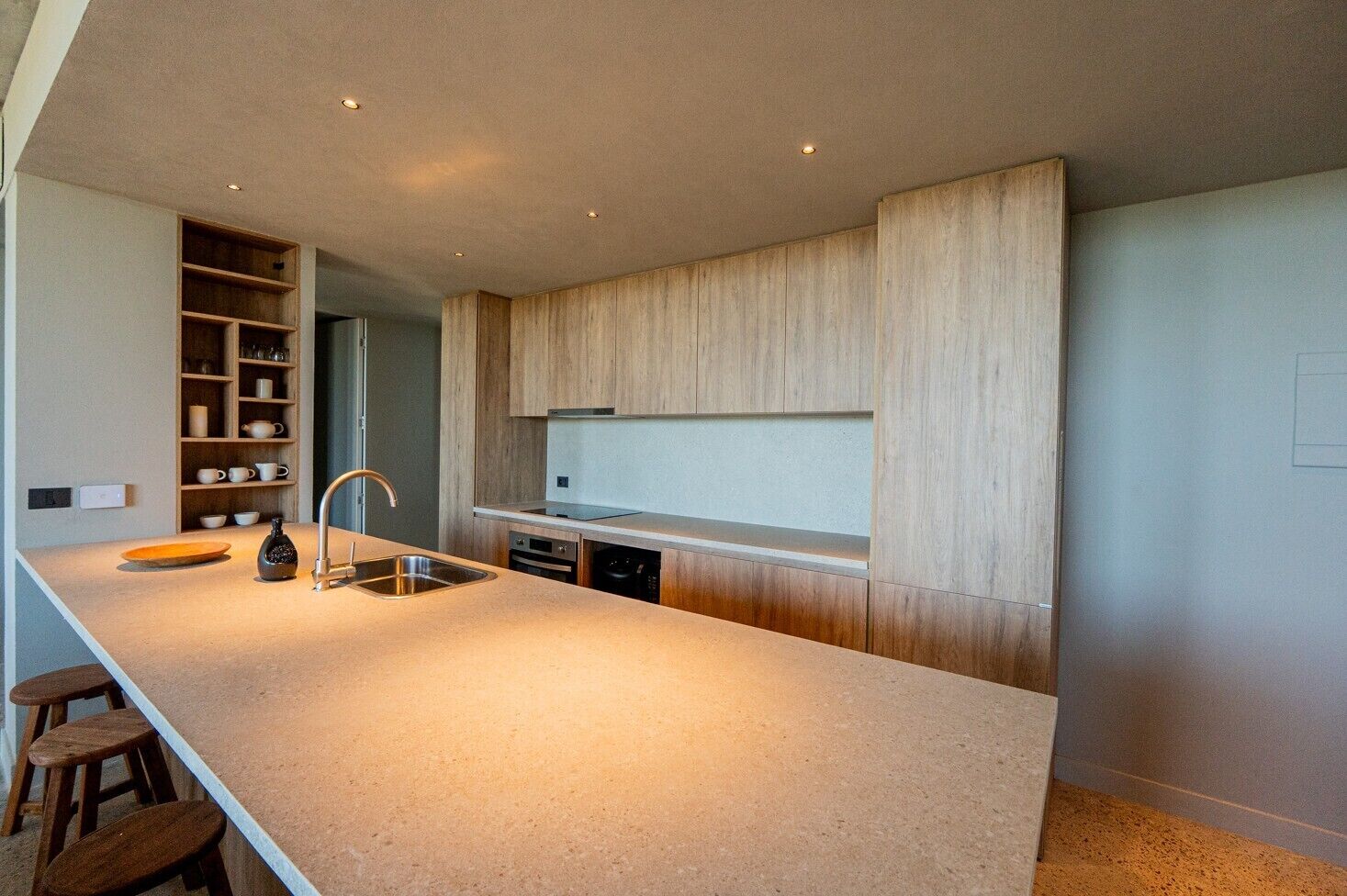 A modern kitchen with a large island, built-in shelves, and a stainless steel sink.