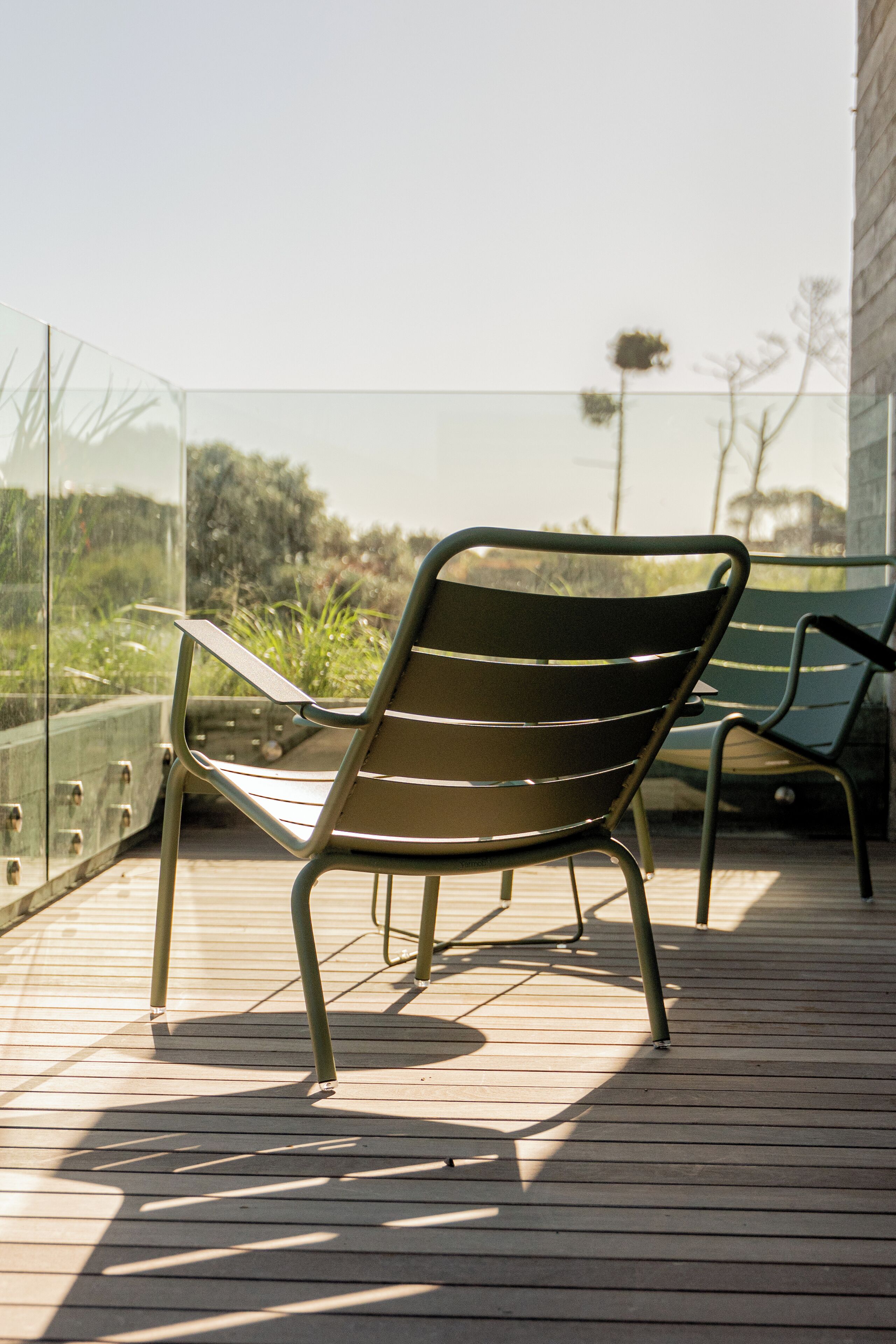Una terraza de madera con una silla de metal y barandilla de vidrio.